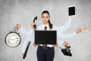 Person im Businesslook mit 6 Händen, die jeweils etwas halten (Telefon, Laptop, Uhr, Hörer, Tablet, Geldscheine)